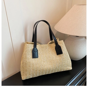 Elegant straw woven tote bag with black handles displayed on a minimalist wooden desk