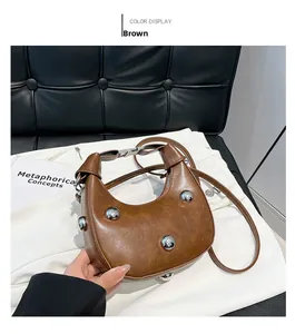 Detail der braunen halbmondförmigen Umhängetasche mit silbernen Nieten auf schwarzem Leder