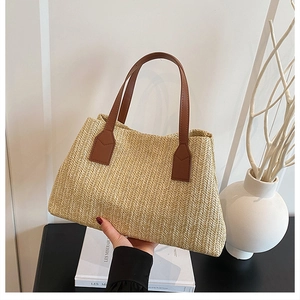 Detail view of a minimalist straw-woven tote bag with stylish brown leather handles