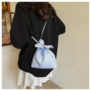 Detail of blue and white checkered drawstring crossbody bag with bow-shaped closure design