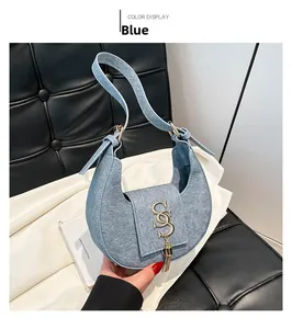 Detalle de bolso medialuna azul con logo metálico dorado y borla sobre tela blanca