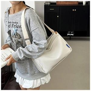 Detail der cremefarbenen Messenger-Tasche mit blauem Label und breitem Gurt am Modell