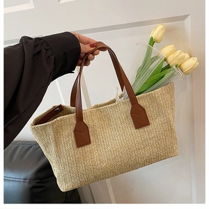 Close-up detail of a stylish woven straw basket handbag with brown leather straps.