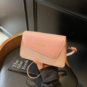 Pink minimalist crossbody square bag with woven texture and gold hardware on leather chair