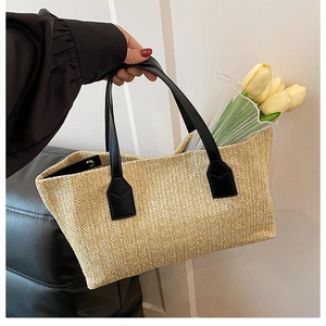 Detail view of a woven straw basket bag with elegant black leather handles and tulips.