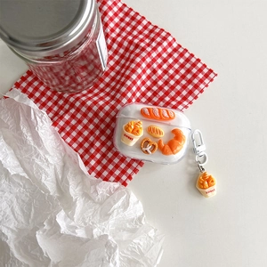 Close-up of AirPods case with 3D miniature bread charms on a red plaid picnic cloth
