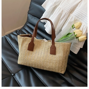 Detail view of a handcrafted straw woven handbag with brown leather straps on a black chair