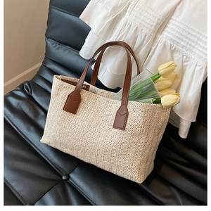 Close-up of a stylish straw woven tote bag with brown leather handles on a chair