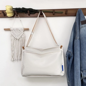 Minimalistische beige Segeltuch Umhängetasche mit blauem Etikett am Holzhaken