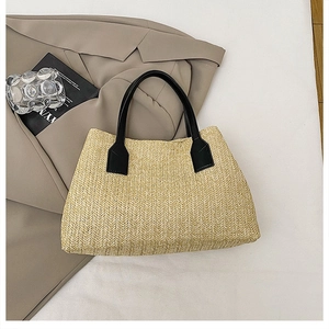 Detail of a natural straw woven handbag with black handles on a beige blazer