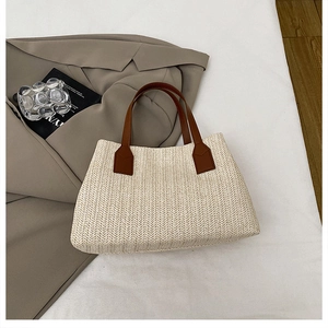 Close-up detail of the elegant beige woven straw handbag featuring brown leather handles