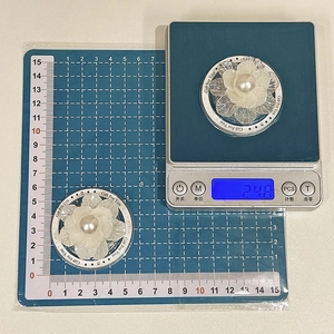 Détail du support de téléphone fleur de perle pesé affichant 24,8g sur une balance