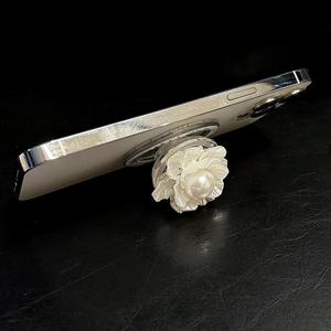 Détail du support de téléphone fleur blanche avec perle montrant la structure pliable sur cuir