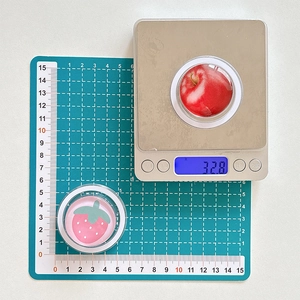 Detail showing strawberry and apple phone grip dimensions and weight on a scale