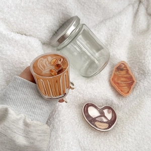 Close-up of coffee and croissant acrylic phone grips on white fleece background