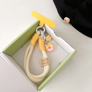 Detail of woven phone strap with yellow star and pink bear donut charm in a gift box