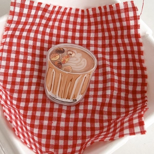 Detail view of a creative latte-shaped acrylic phone grip on a red plaid picnic background