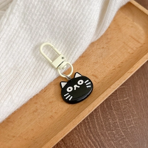 Detail of a black cartoon cat charm with a white lobster clasp on a wooden tray