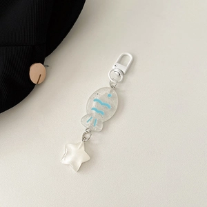 Detail of cute fish pendant with blue waves and white star charm on a cream background