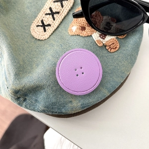 Detail of blue denim fabric featuring bear embroidery and a purple round leather button