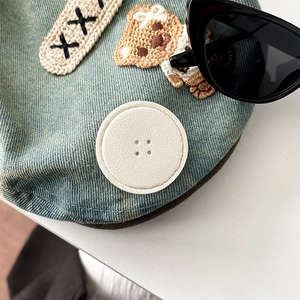 Detail shot of denim phone socket featuring a brown teddy bear embroidery and button patch