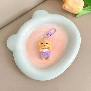 Détail d'un pendentif chiot jaune avec salopette violette dans un plateau en céramique