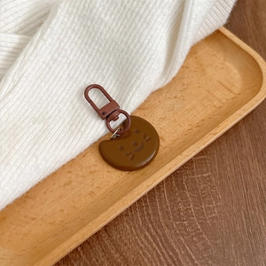 Close-up of a brown resin bear keychain with a matching lobster clasp on a wooden tray