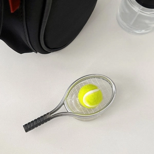 Macro shot of mini silver tennis racket and yellow ball keychain on black bag