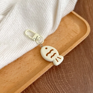 Detail of a beige Taiyaki fish charm with lobster clasp on a wooden tray