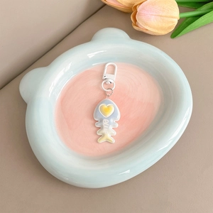 Detail of cute blue and yellow fishbone charm with heart on a ceramic bear tray