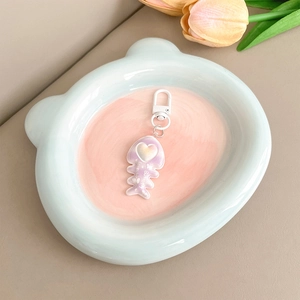 Detail of pink gradient fishbone keychain with heart and white metal clasp on blue plate