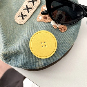 Detail of blue denim accessory featuring yellow button and cute bear embroidery patch