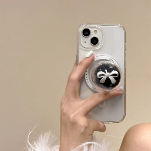 Detail view of a phone grip with a silver bow and black pom-pom in a clear sphere