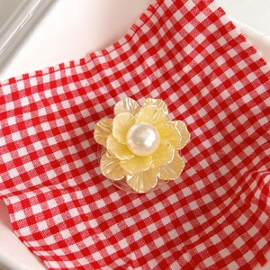 Detail of yellow flower phone grip with cream petals and center pearl on checkered cloth