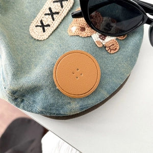 Detail of light blue denim phone grip with cute bear embroidery and brown leather patch