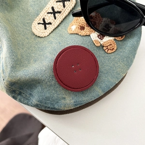 Detail of blue denim phone grip with leather patch, bear embroidery, and button texture