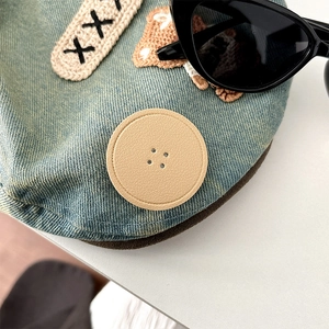 Detailed macro shot of light blue denim hat featuring bear embroidery and leather button