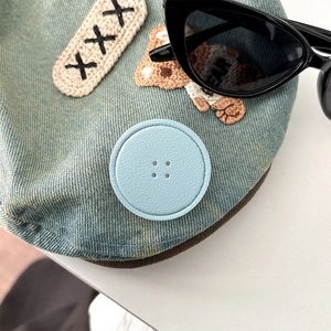 Detail of light blue denim fabric with embroidered bear patch and round leather button