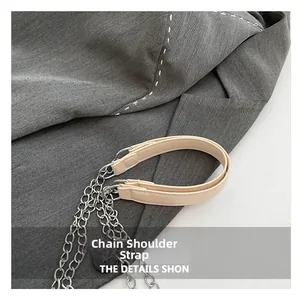 Detail view of silver metal chain strap with beige leather shoulder pad and fine stitching