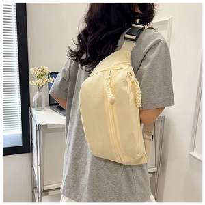 Detail of light yellow crossbody bag featuring woven rope zipper pulls and nylon strap