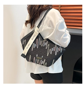 Close-up of black quilted tote bag featuring colorful wavy embroidery and wide logo strap
