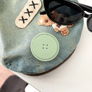 Close-up of light blue denim accessory with mint green faux leather button and embroidery