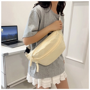 Detail of light beige canvas sling bag featuring dual zippers and adjustable buckle strap