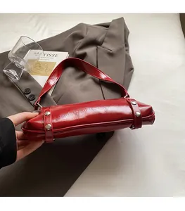 Detailed side view of glossy red leather shoulder bag with silver rivet reinforcements
