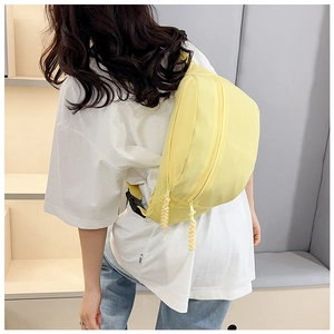 Detail of light yellow canvas chest bag with woven zipper pull and black buckle straps