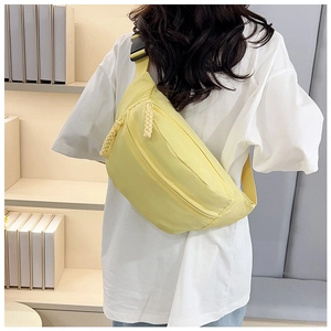 Detail of pale yellow minimalist crossbody bag with woven zipper pull and plastic buckle