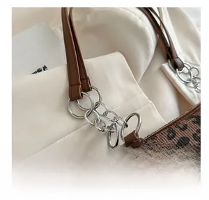 Detail of silver metal chain links and brown leather strap on a leopard print tote bag