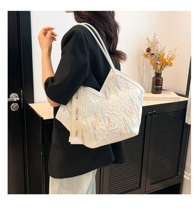Detail of colorful embroidery and branded wide strap on white large capacity tote bag