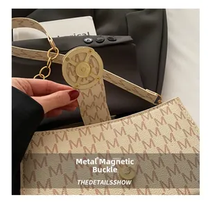 Detail view of the golden magnetic buckle closure on a monogrammed underarm bag