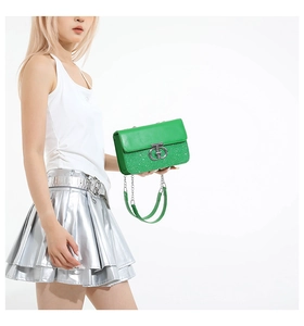 Close-up of green sequin handbag featuring silver logo and metal chain shoulder strap